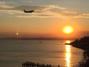 Silhouette airplane flying over sea against sky during sunset