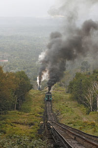 Two steam locomotives of mount washington cog railway pusing up coaches to  summit at good weather .