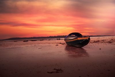 Boat moored on beach against sky during sunset