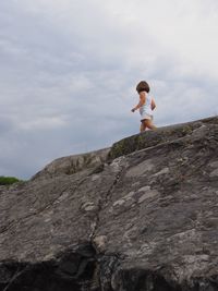 Low angle view of girl walking on rock against sky