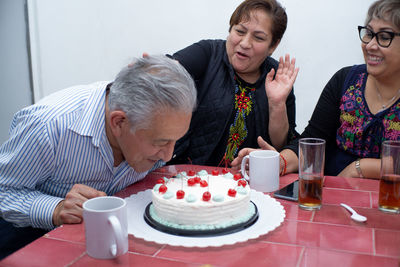 An older man with his friends celebrating his birthday, biting his cake at an indoor party