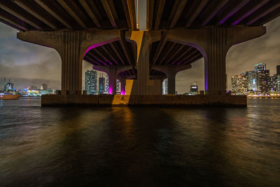 Underneath view of bridge over river in city at night