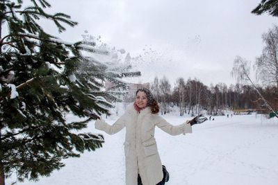 Young woman throwing snow while standing on land during winter