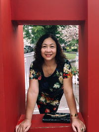 Portrait of smiling young woman standing against red wall