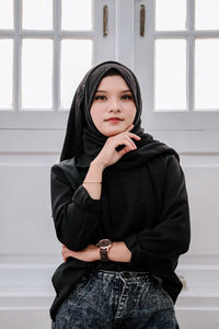 Portrait of young woman standing against window