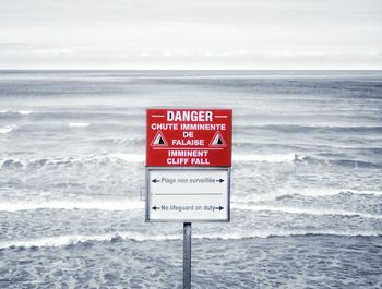 Warning sign by sea against sky