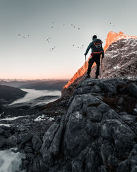 Man on rock in mountains against sky during sunset