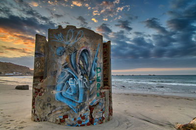 Graffiti on beach against sky during sunset
