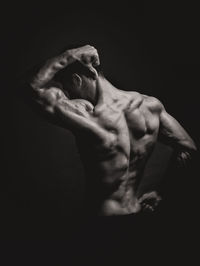 Rear view of shirtless body builder flexing muscles against black background
