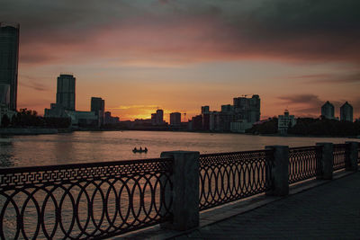 Buildings by river against sky during sunset