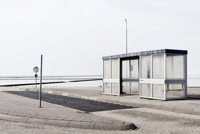 Empty street by sea against clear sky