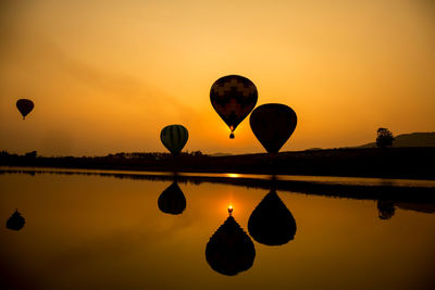 Silhouette hot air balloons in lake against sky during sunset