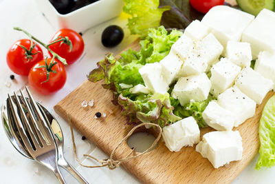 Cooking qreek salad with fresh vegetables, feta cheese and black olives on a white wooden table.