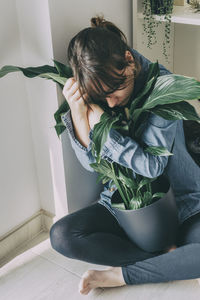 Woman sitting on potted plant at home