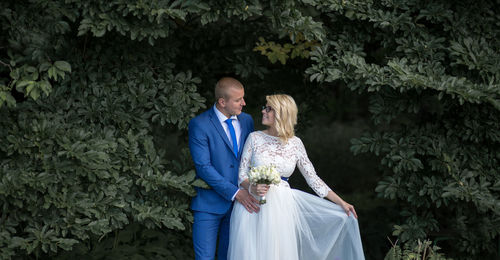 Bridal couple looking at each other while standing amidst tree branches at park