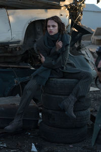 Thoughtful young woman sitting on stacked tire at junkyard