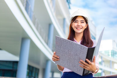 Portrait of young woman holding smart phone while standing outdoors