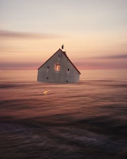 Small house sinking in the sea during sunset