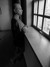 Side view of young woman looking through window at home