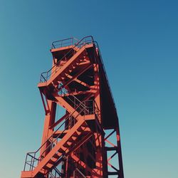 Low angle view of stairs on metallic structure against clear blue sky