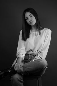 Portrait of woman sitting against black background