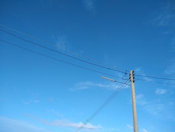 Low angle view of electricity pylon against blue sky