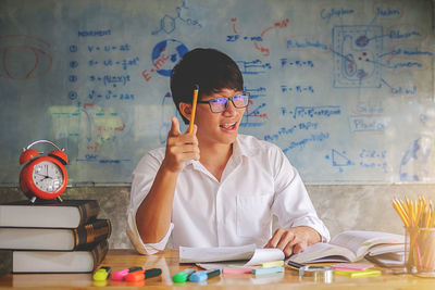 Portrait of cheerful man studying at desk against whiteboard