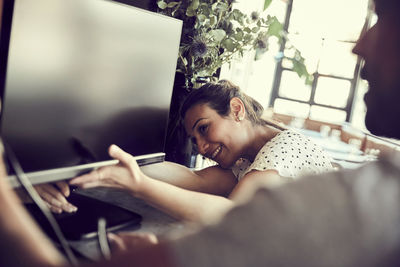 Smiling female with male owner adjusting cable of computer monitor in cafe