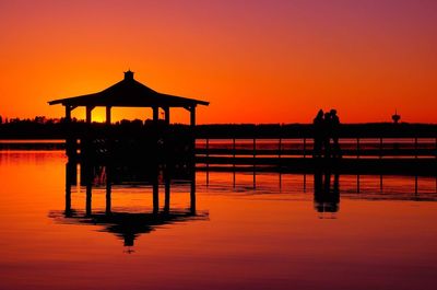 Silhouette pier on sea against orange sky