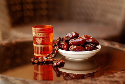 An oriental drink, an arabic rosary, and dates on a white plate stand on a glass table.