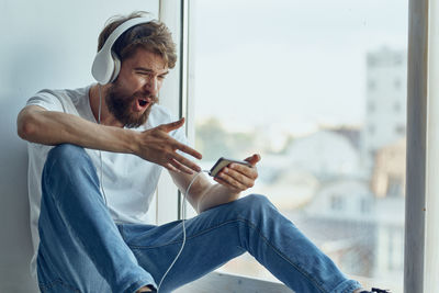 Midsection of man using mobile phone while sitting on window