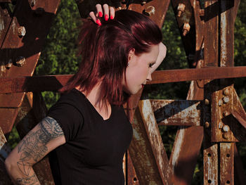 Side view of young woman looking away while standing by fence