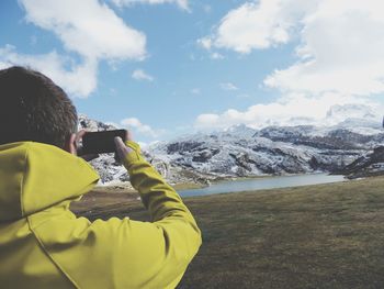 Rear view of man photographing on snowcapped mountains