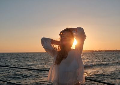 Woman standing by sea against sky during sunset