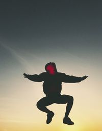 Silhouette of man jumping with arms outstretched against sky during sunset
