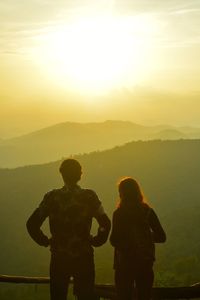 Rear view of people standing on mountain against sky during sunset