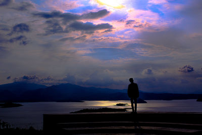 Rear view of silhouette man standing on mountain against sky during sunset