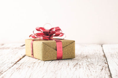 Close-up of christmas present on wooden table against wall