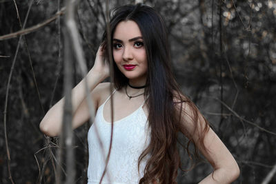 Portrait of beautiful young woman standing against tree