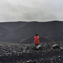 Rear view of woman sitting on rock against volcanic mountain