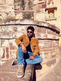 Portrait of young man sitting against wall