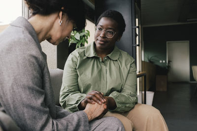 Businesswoman consoling mature female colleague while holding hands at office