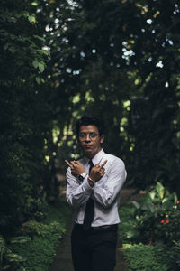 Young man standing by trees in forest