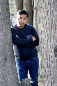 Portrait of young man leaning on tree trunk