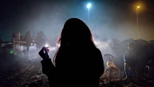 Rear view of silhouette woman standing against sky at night