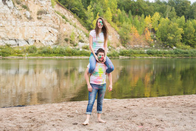 Man carrying woman on shoulders while standing against lake