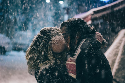 Close-up of couple kissing on street while snowing