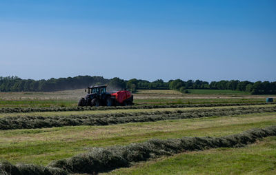 Black tractor with a red straw chamber press during the straw harvest on a mown field