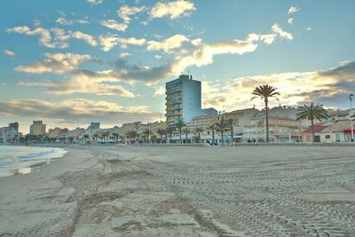 Beach by buildings against cloudy sky