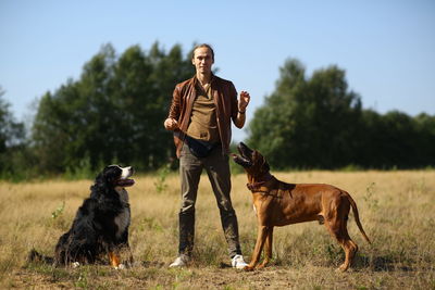 Portrait of man training dogs on land against clear sky